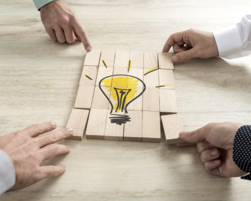 Conceptual of business strategy, creativity or teamwork Four businessmen holding pieces of a wooden bricks bearing the image of a light bulb conceptual of business strategy, creativity or teamwork.